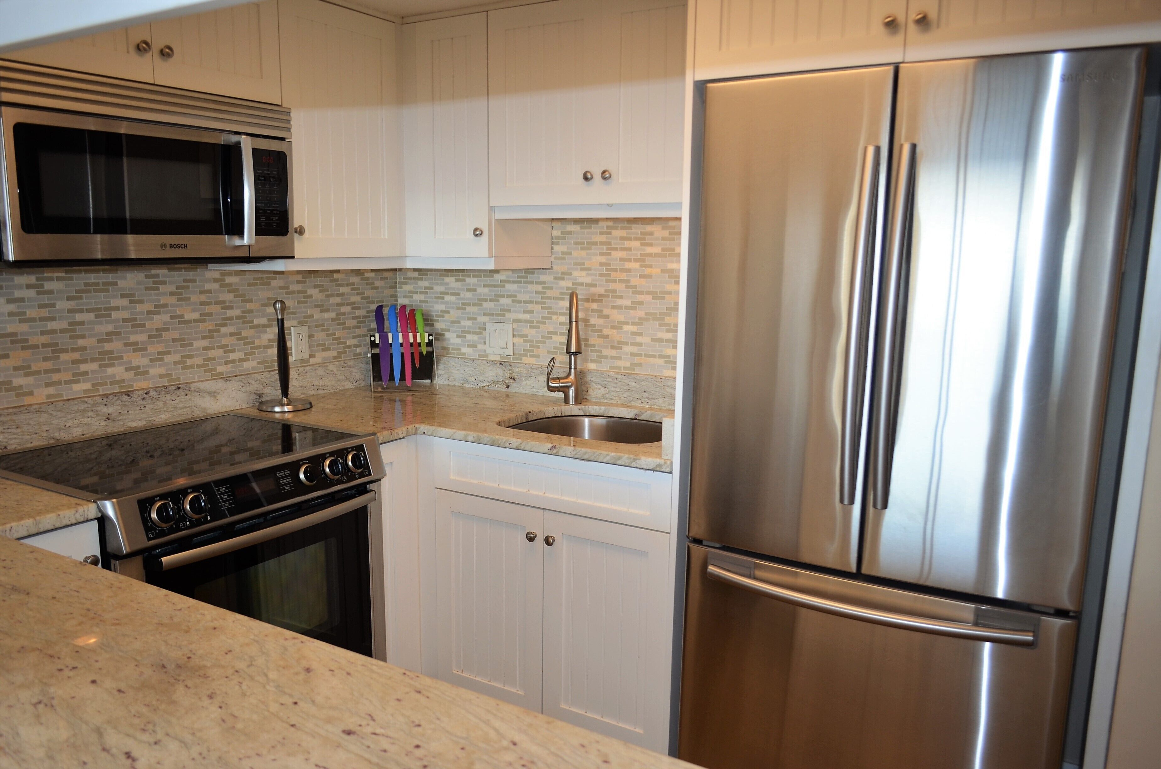 Una cocina con electrodomésticos de acero inoxidable, microondas, estufa, horno y refrigerador.