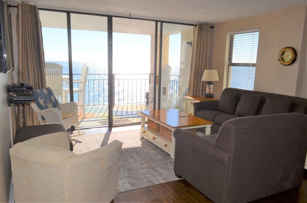 Un soggiorno con divano, poltrone, tavolino e televisore. Include un balcone con vista sul mare.