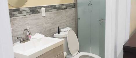 Un baño pequeño con un lavabo blanco, un inodoro y una cabina de ducha con mampara de vidrio.