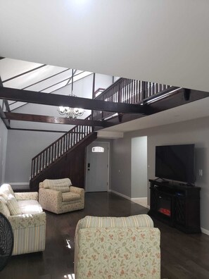 A spacious living room with a high ceiling, a staircase, a chandelier, a television, and two patterned armchairs. - home away from home close to lake and marina (Mayfield)