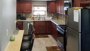 Una cocina con armarios de madera, un refrigerador de acero inoxidable, una estufa y un comedor con mesa y sillas.