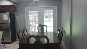 Un comedor con una gran mesa de madera y sillas, un candelabro y un refrigerador al fondo.