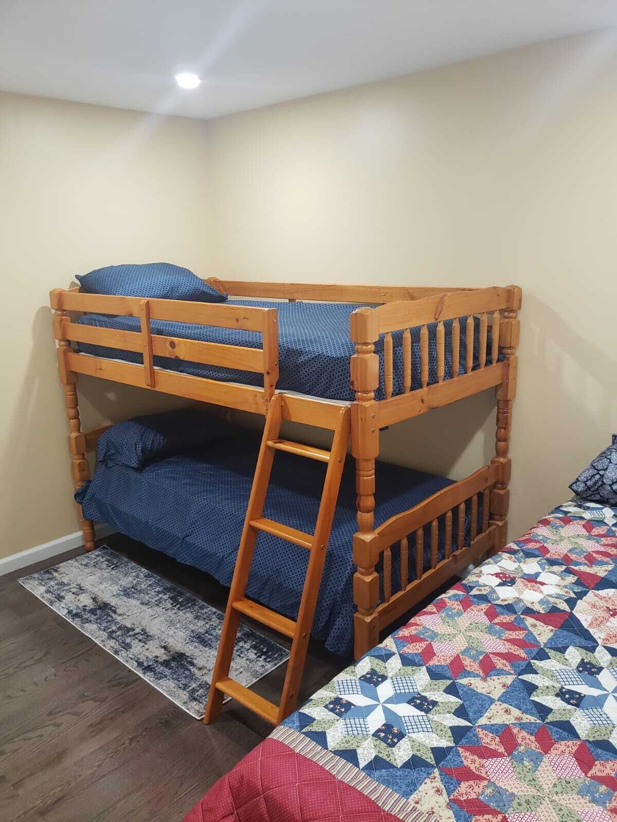 A bunk bed with a ladder, a patterned quilt, and a rug on a wooden floor.