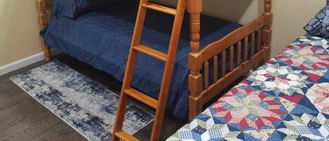 A bunk bed with a ladder, a patterned quilt, and a rug on a wooden floor.