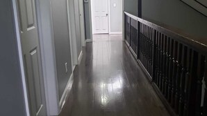 Un pasillo con suelo de madera, puertas blancas y barandilla negra.