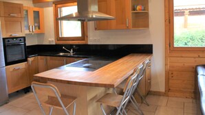 Una cocina moderna con armarios de madera, campana extractora de acero inoxidable, encimera negra y una zona de bar con taburetes.