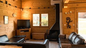 Un interior de cabaña acogedor con chimenea, paredes de madera, televisor y sofá.