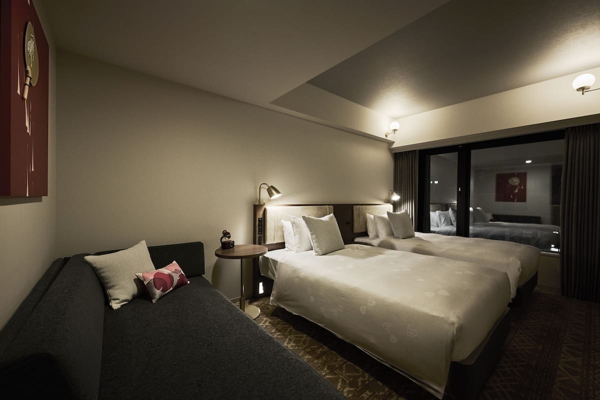 A hotel room with two beds, a small table, and a nightstand.