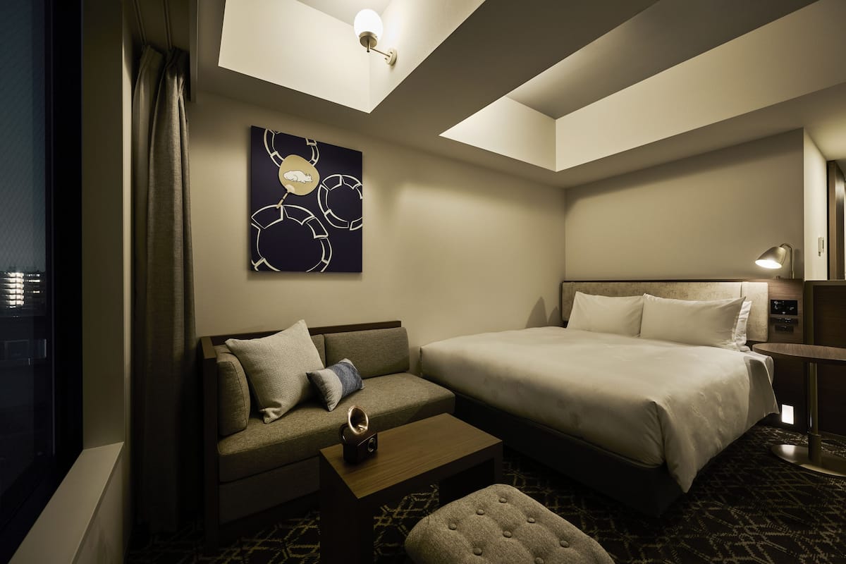 A hotel room with a bed, a sofa, a coffee table, and a wall-mounted artwork.