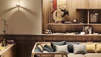 A cozy living room with a sofa, decorative pillows, a wooden cabinet, and a wall-mounted shelf with books and a vase.