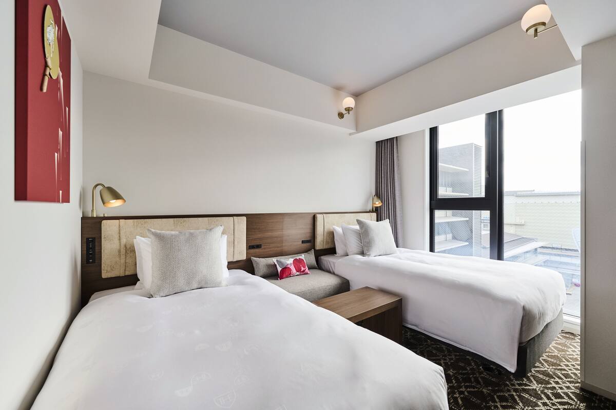 A hotel room with two beds, a wooden headboard, a small table, and a large window offering a view.
