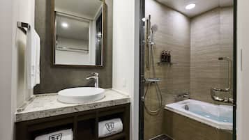 A modern bathroom with a marble sink, a large mirror, a glass-enclosed shower, and two towels with a logo.