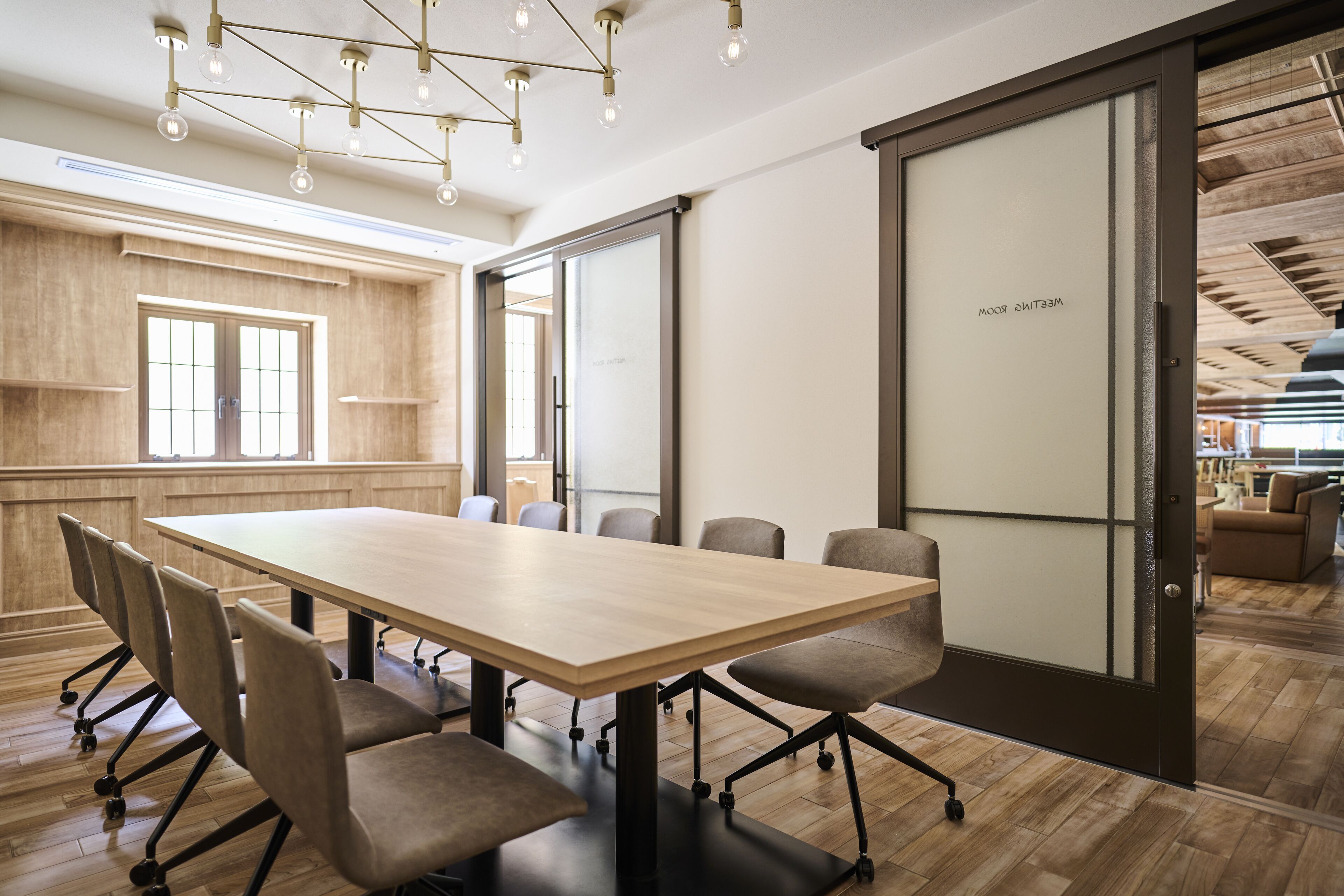 Un salón de conferencias con una gran mesa, sillas y una puerta corredera con la leyenda 'Welcome Room'.
