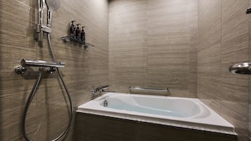 A modern bathroom with a freestanding bathtub, a handheld showerhead, and a glass shelf with toiletries.