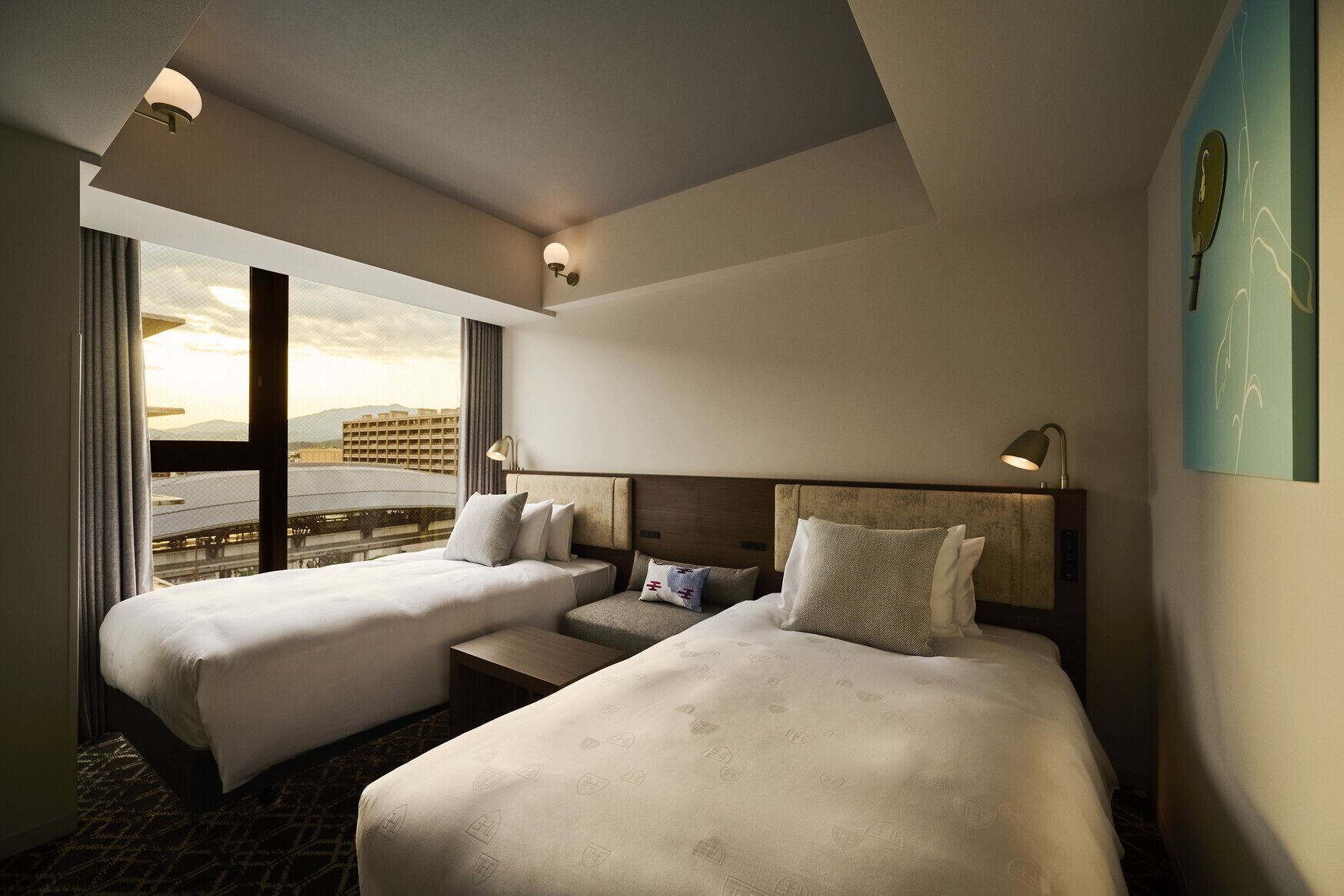 A hotel room with two beds, a nightstand, a lamp, and a view of the cityscape.