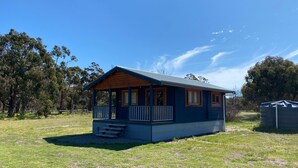 A small, single-story cabin with a porch, surrounded by grass and trees.