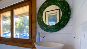 A bathroom with a white sink, wooden countertop, and a green mosaic mirror.