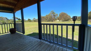 A covered porch with a view of a grassy field and trees.