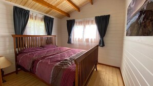A bedroom with a wooden bed, a window with curtains, and a painting on the wall.