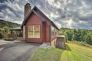 A log cabin with a stone chimney, a porch with outdoor seating, and a view of a forested hillside. - Family Blue Ridge Gem w/ Hot Tub! 1/2 Mi to River (Piney Creek)