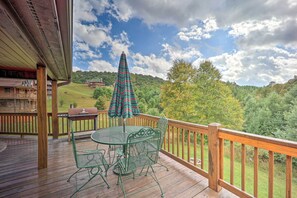 A wooden deck with a glass table and chairs, a striped umbrella, and a view of a green landscape. - Family Blue Ridge Gem w/ Hot Tub! 1/2 Mi to River (Piney Creek)