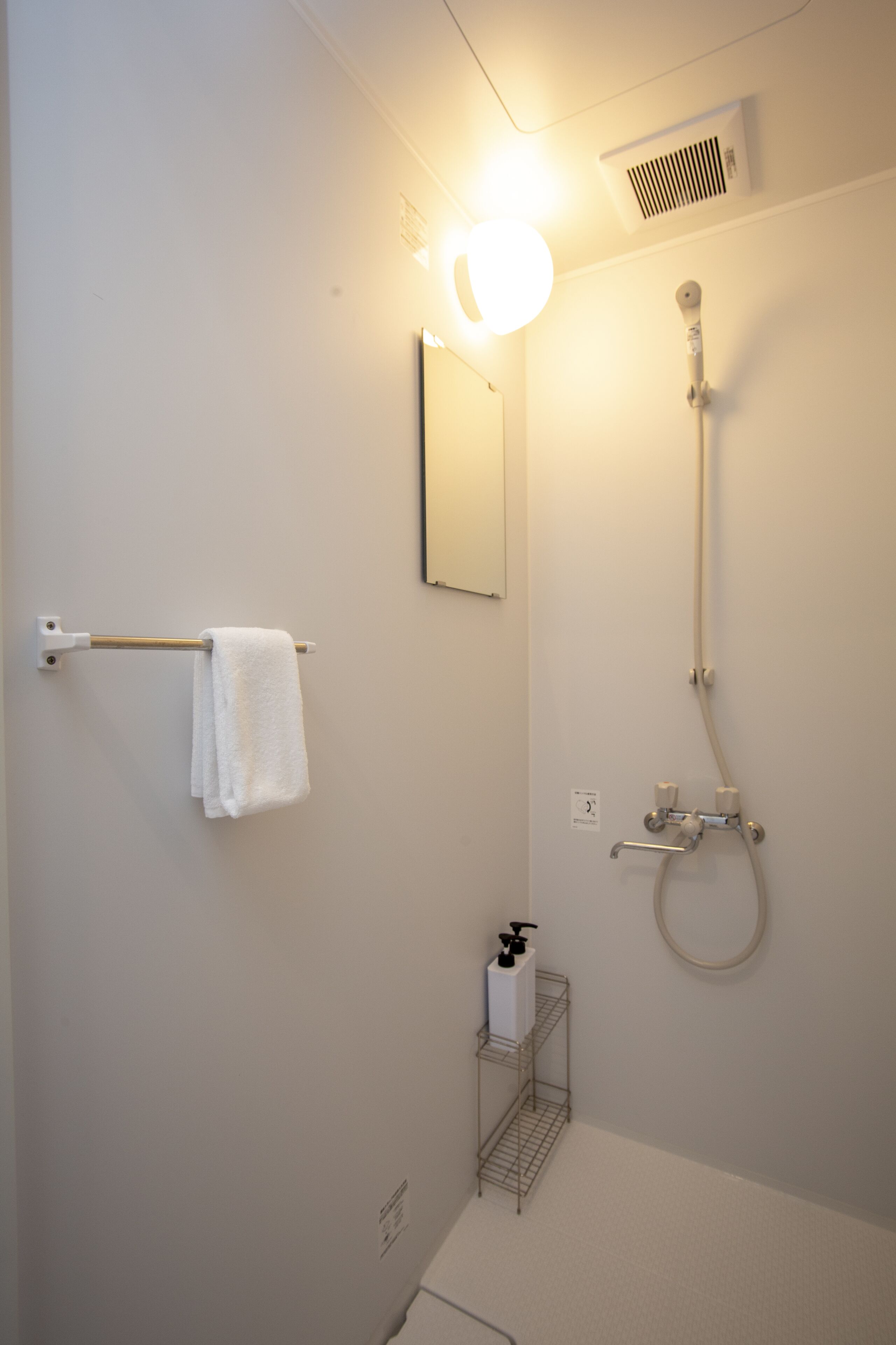 Ett badrum med en handduksställning, en dusch, en spegel och en hylla med toalettartiklar.