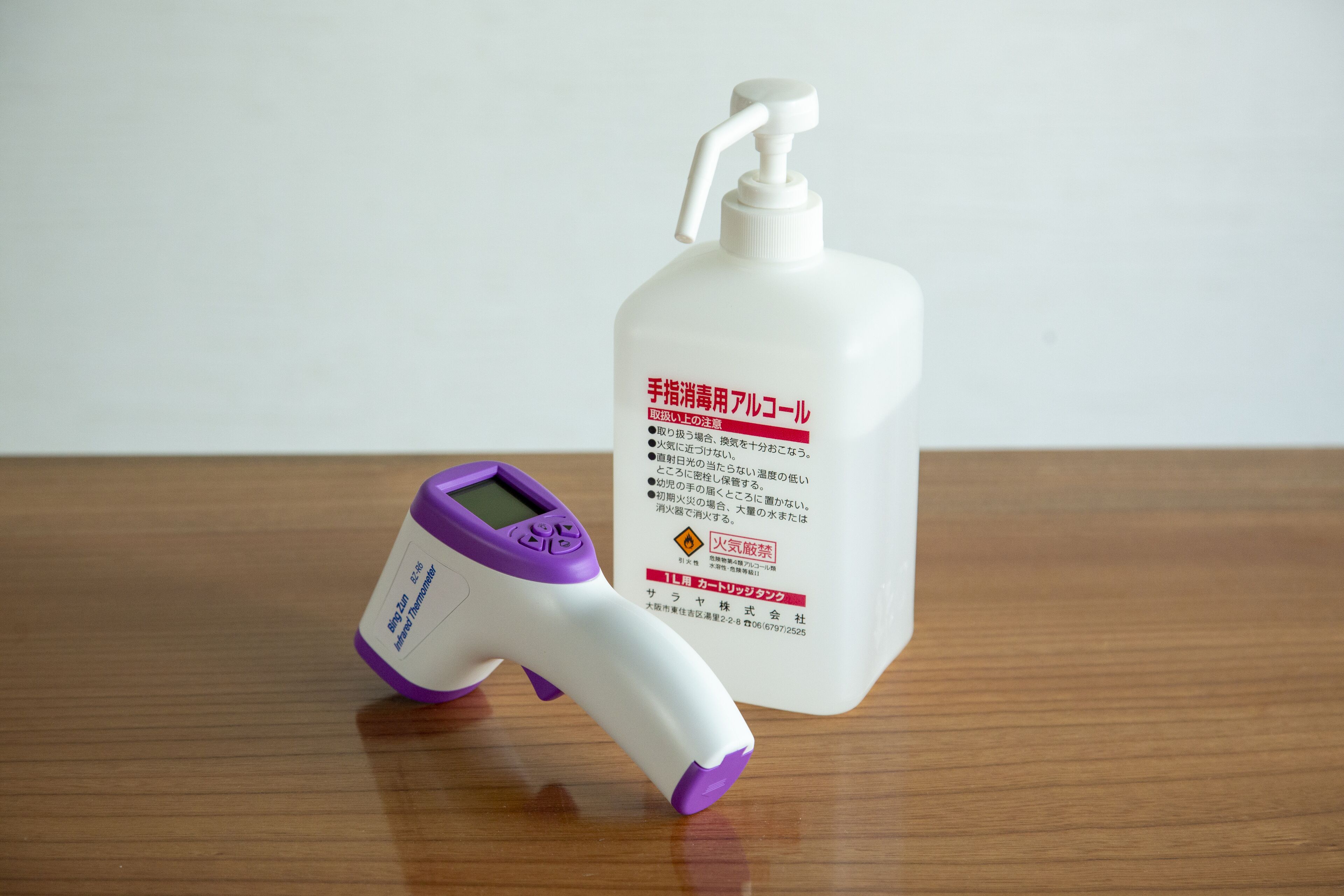 Un termómetro digital y una botella de desinfectante para manos sobre una superficie de madera.
