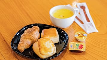 Een bord met croissants, een kom soep en een klein potje jam op een houten tafel.