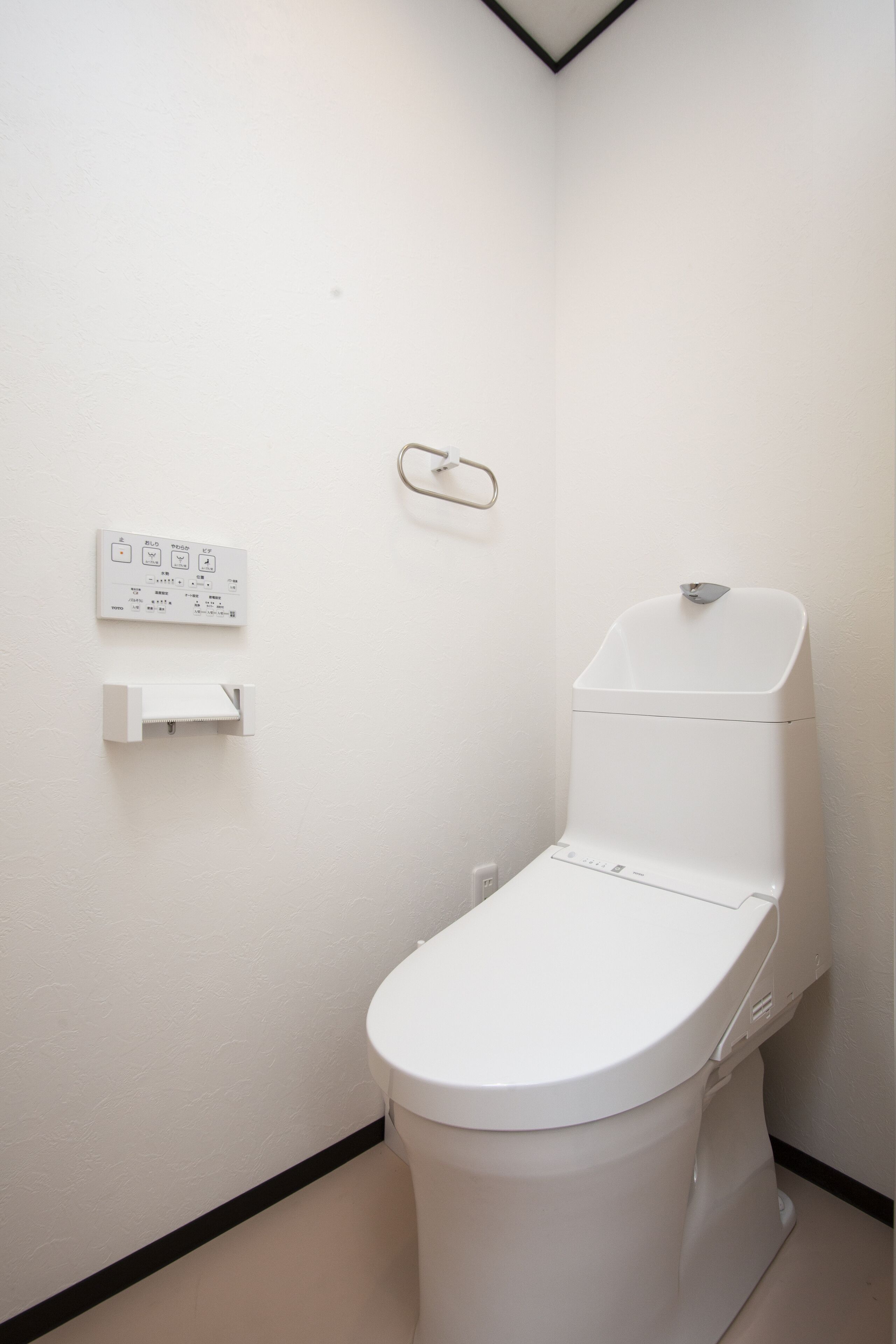 Un bagno piccolo e bianco con un water, un asciugamani ad aria e una presa elettrica a muro.