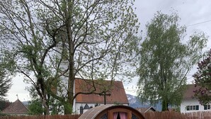 A rustic wooden barrel house with a checkered curtain, a round table, and a bench in a garden setting. - Vacation home (Eisenberg)