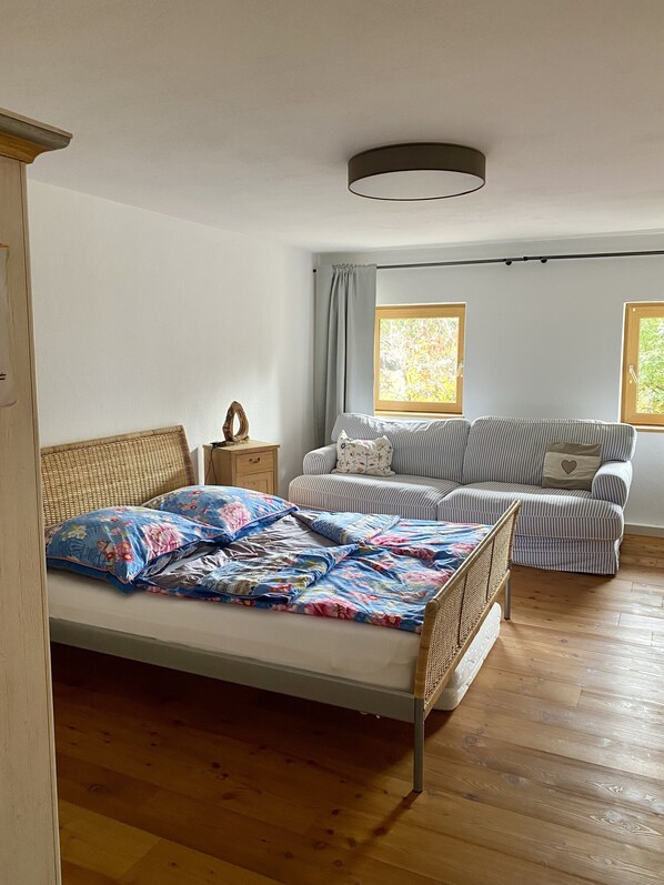 A bedroom with a bed, a sofa, a nightstand, and a window.