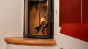 A corner room with a fireplace, a red cushioned bench, and a small shelf with a tin. - Vacation home (Eisenberg)
