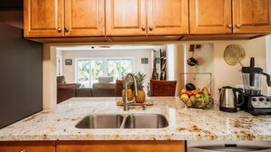 Una cocina con armarios de madera, encimera de granito, lavamanos doble, frutero y cafetera.