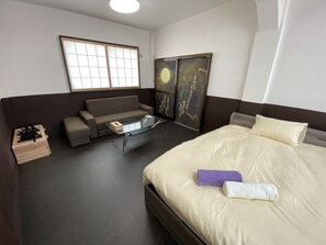 Ett hotellrum med en säng, en soffa, ett soffbord i glas, en trälåda och ett fönster med utsikt över himlen.