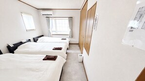 Quarto de hotel com três camas, janela com cortinas, unidade de ar condicionado e placa de saída fixada na parede.