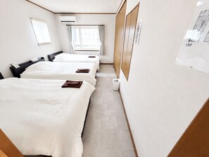 Habitación de hotel con tres camas, una ventana con cortinas, un equipo de aire acondicionado y un letrero de salida instalado en la pared.