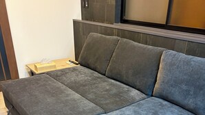 Una habitación moderna con un sofá gris, una mesita de madera y un panel de control en la pared.