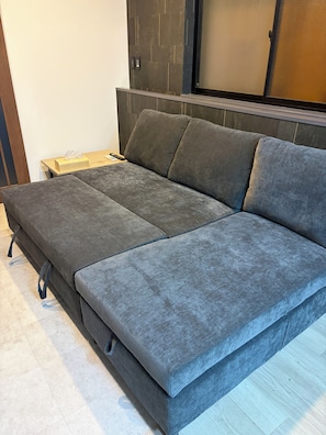 A modern room with a grey sofa, a wooden side table, and a wall-mounted control panel.