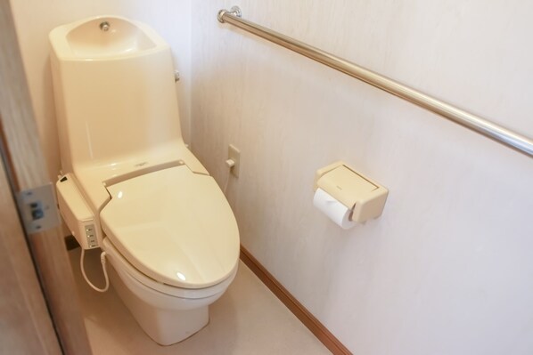 Inodoro con asiento bidé, barra de apoyo y soporte para papel higiénico.