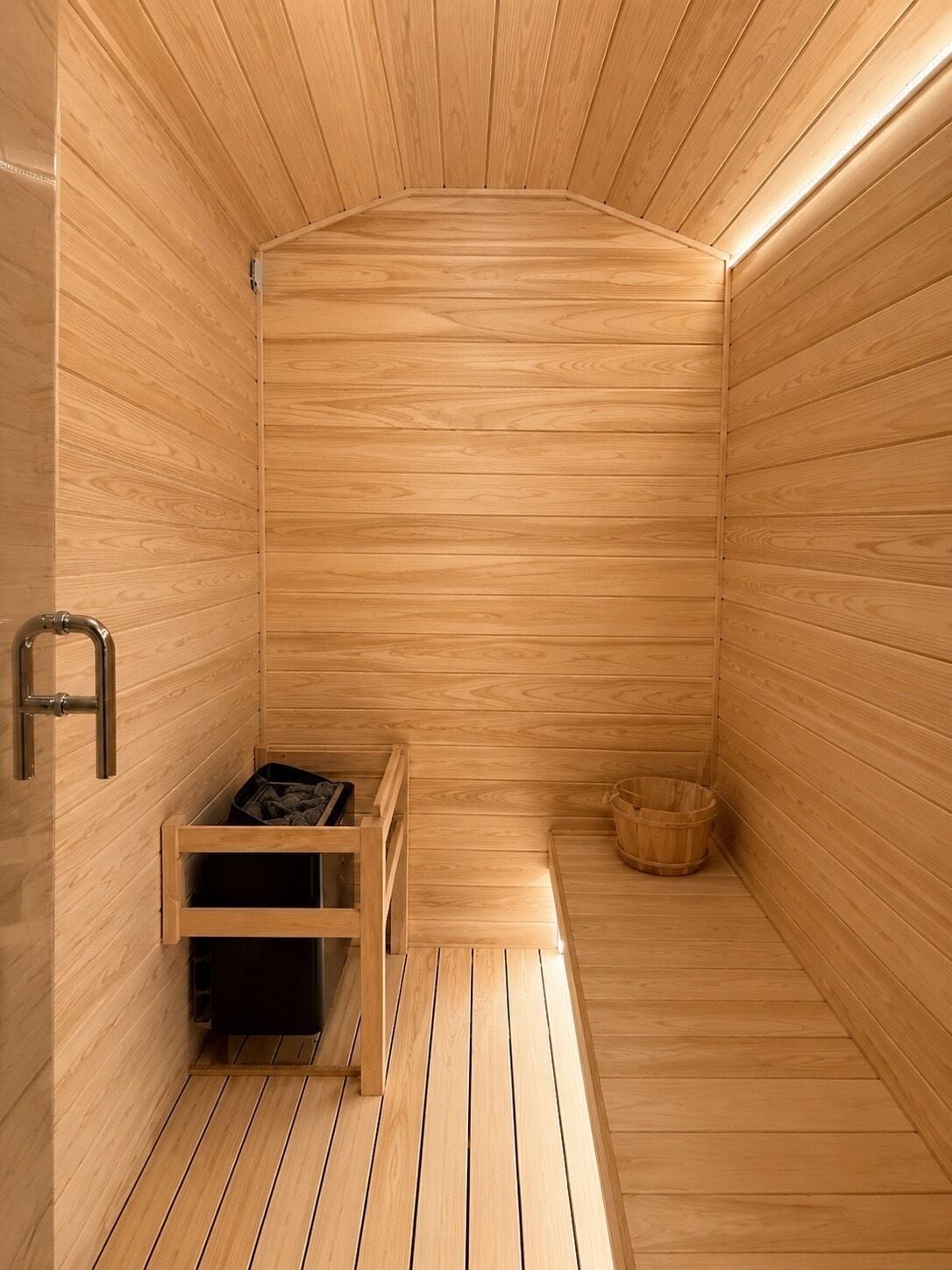 A sauna with wooden walls and floor, a bench, a small table, and a trash bin.