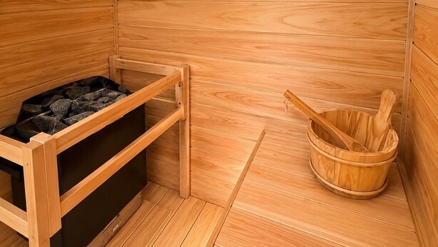 Un sauna con un banco de madera, un mueble de almacenamiento negro y un balde de madera.