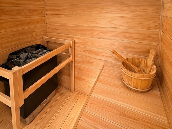 A sauna room with a wooden bench, a black storage unit, and a wooden bucket.