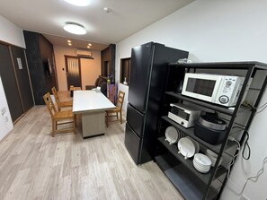Cocina compacta con una mesa de comedor, sillas, un refrigerador negro, un microondas y una estantería con vajilla.