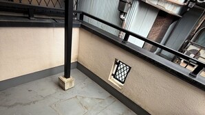 Varanda de concreto com guarda-corrimão de metal, uma pequena grelha de ventilação e um aparelho de ar condicionado fixado na parede.