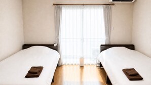 Quarto de hotel com duas camas, piso de madeira e janela com cortinas.