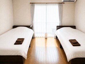 Una habitación de hotel con dos camas, piso de madera y ventana con cortinas.