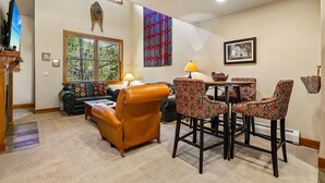 A living room with a sofa, a coffee table, patterned chairs, a TV, a window, and a wall hanging.