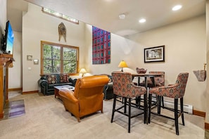 A living room with a sofa, a coffee table, patterned chairs, a TV, a window, and a wall hanging.