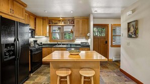A kitchen with wooden cabinets, a black refrigerator, a stove, and a window with blinds.