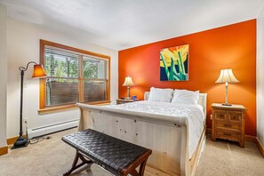 A bedroom with a bed, bedside tables, a bench, and a window with blinds.